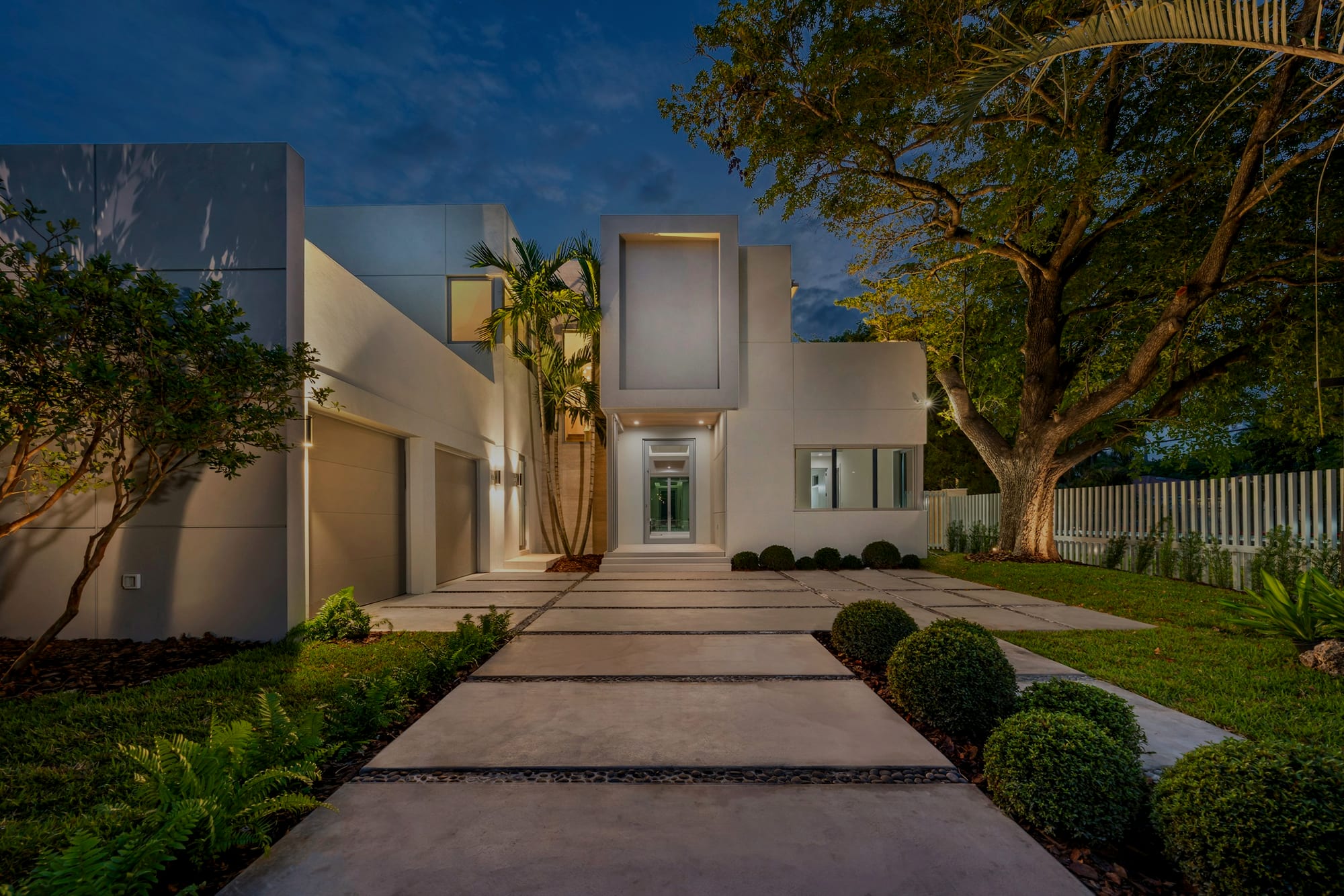 The entry drive at dusk, clipped hedge either side, the house lit beyond.