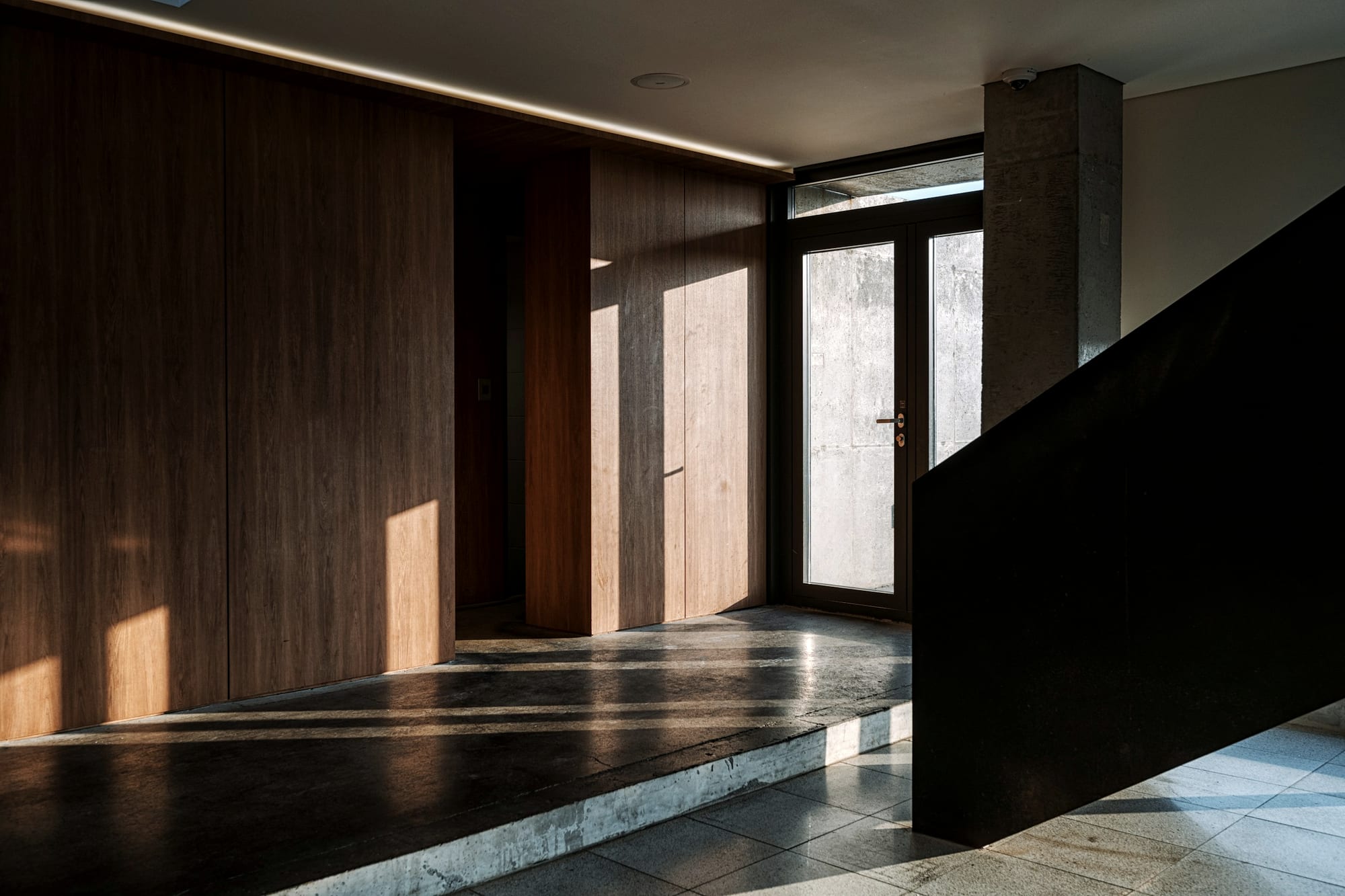 The entrance hall, walnut panelling and honed travertine, lit from one side.