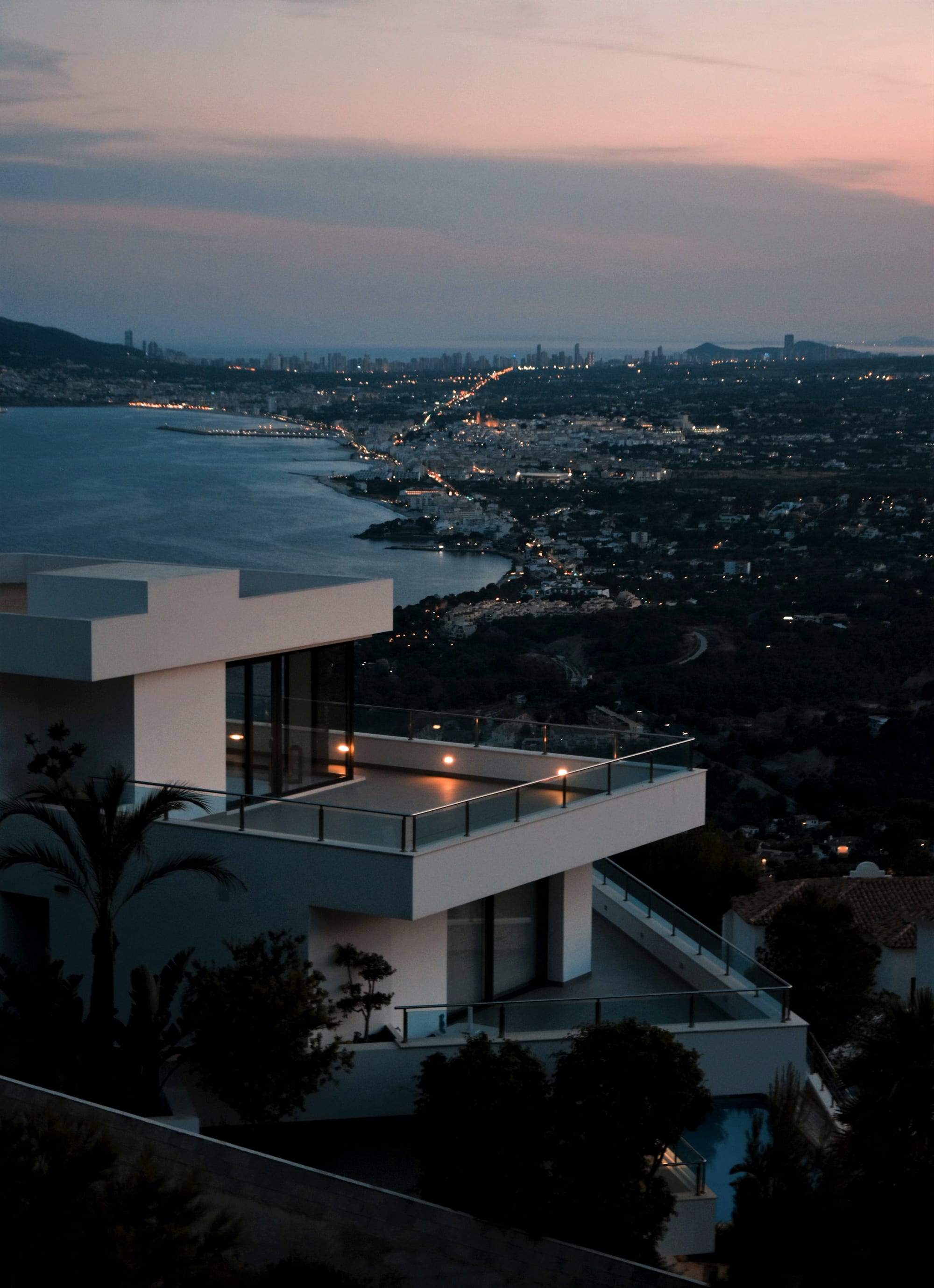 A terrace above the water at dusk, the coast lit below.