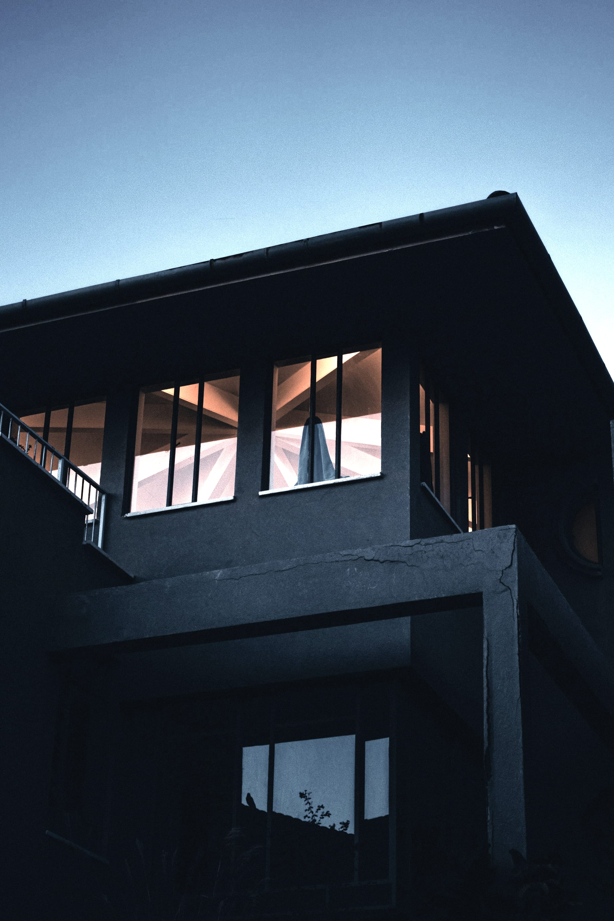 A dark modern building at dusk, upper floor windows lit.